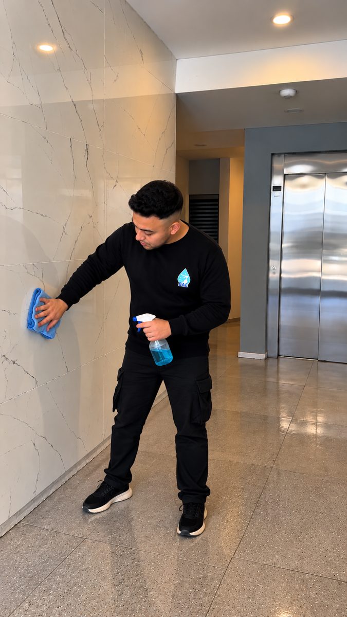 Personal de BAE uniformado limpiando una pared de mármol en el hall de un edificio